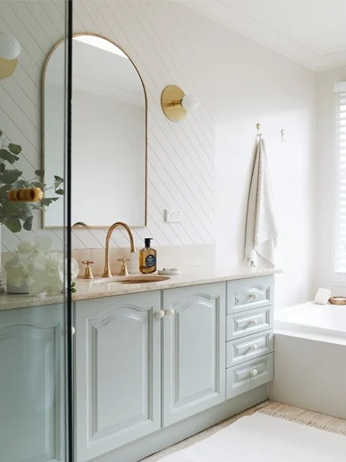 Renovated bathroom with gold fixtures and soft green cabinetry