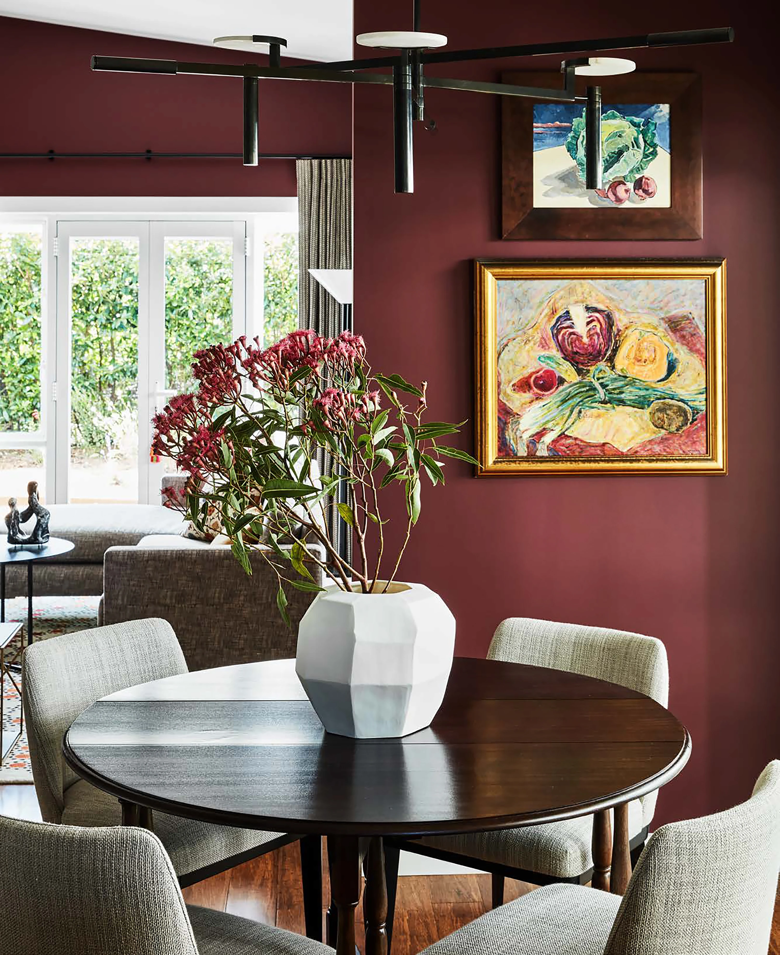Dining toom with round table, four chairs, paintings, on maroon wall