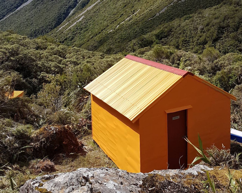 Sir Robert Hut is bright orange and sits on a stony mountain which also has grasses covering it