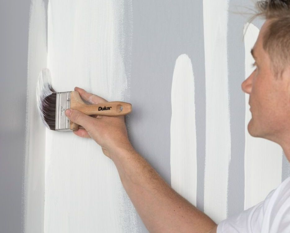 Man using a paint brush to cut in wall paint into a corner