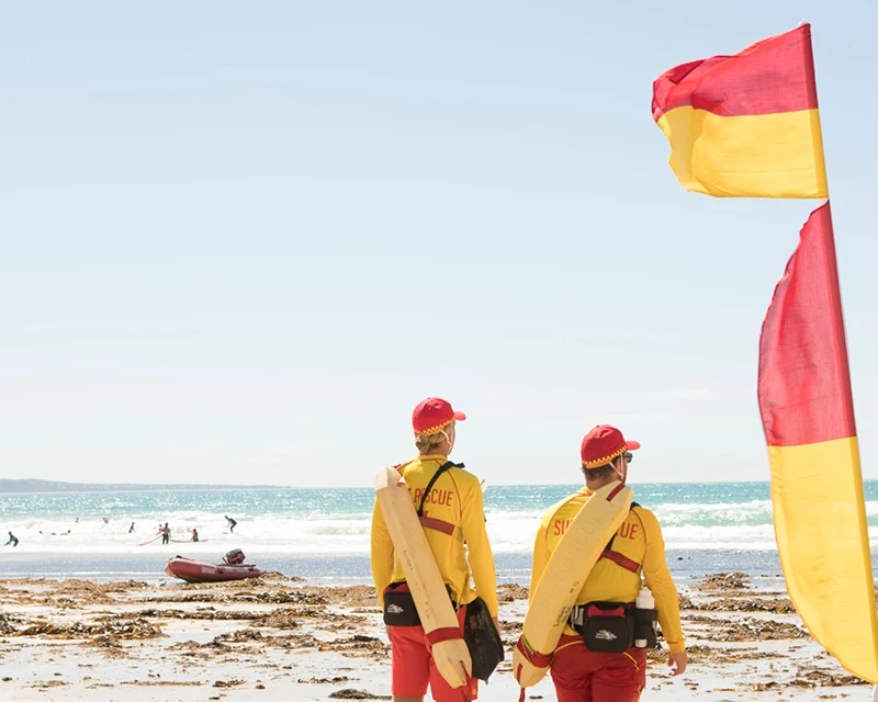 Surf Life Savers watching the people swimming in the beach, next to the red and yellow flag.