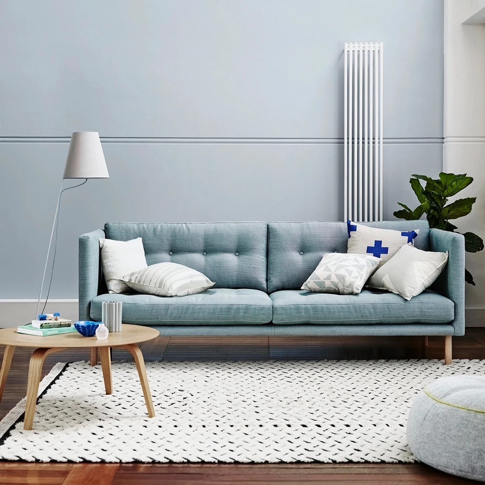 Blue grey wall and blue couch with cushions, timber floor, timber coffee table.