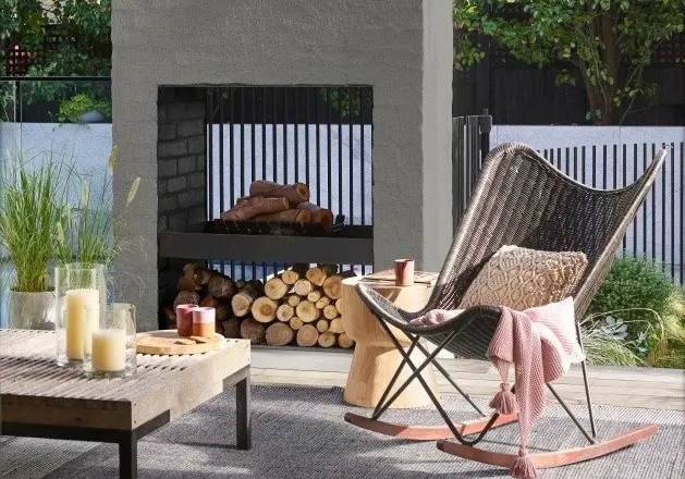 Outdoor entertaining area with open fireplace, chair and low wooden coffee table.