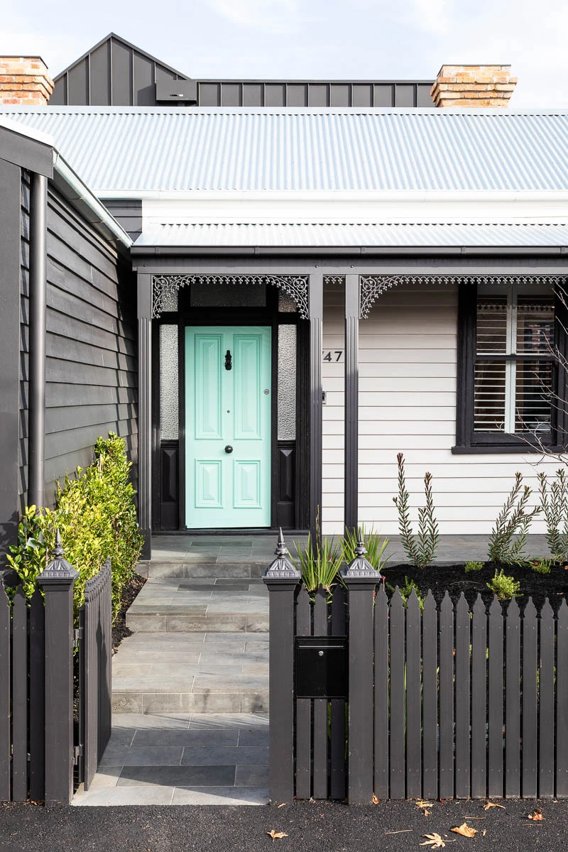 View from street of dark picket fence home with light green door.