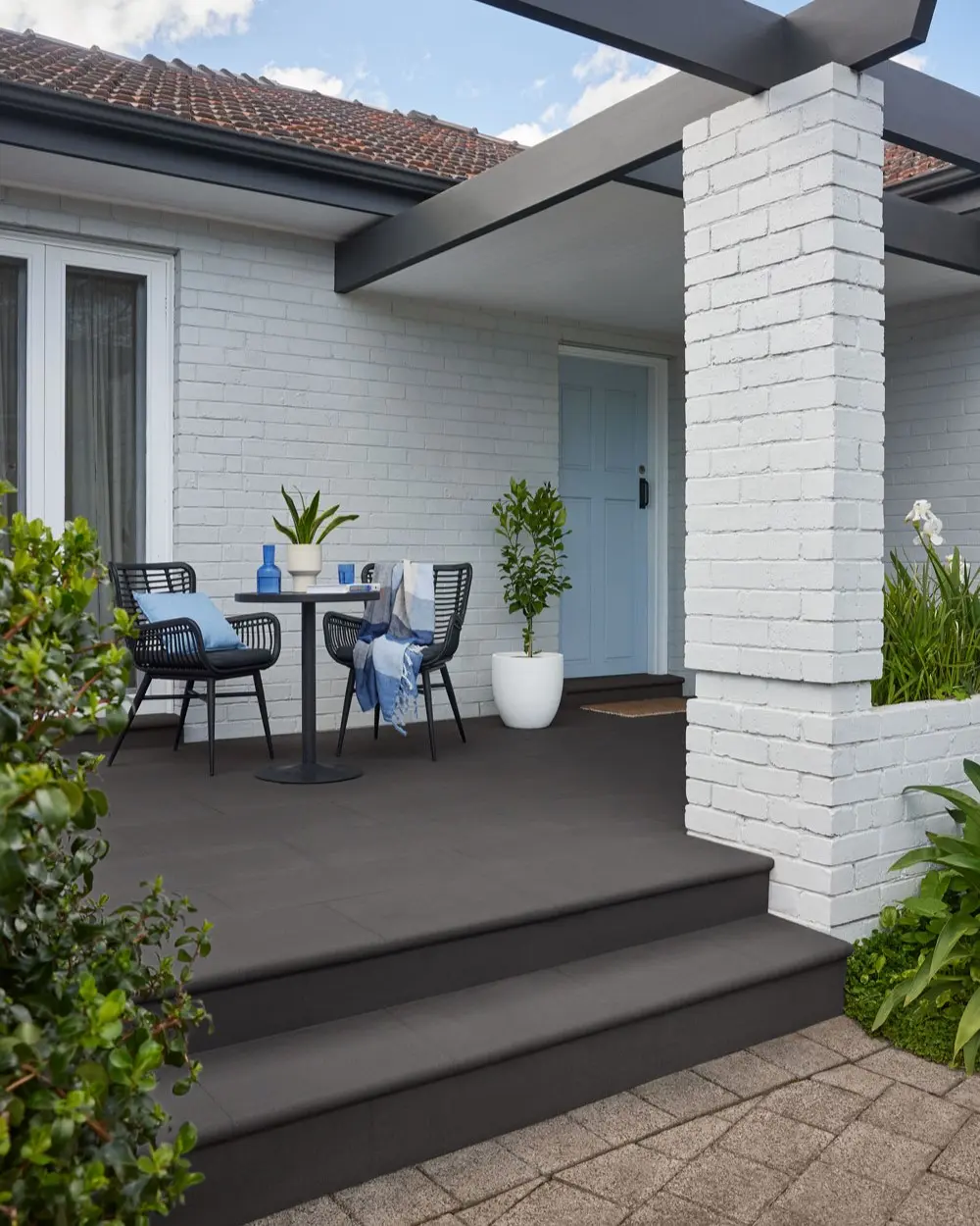 Pavers painted grey at patio entry of a white brick house.