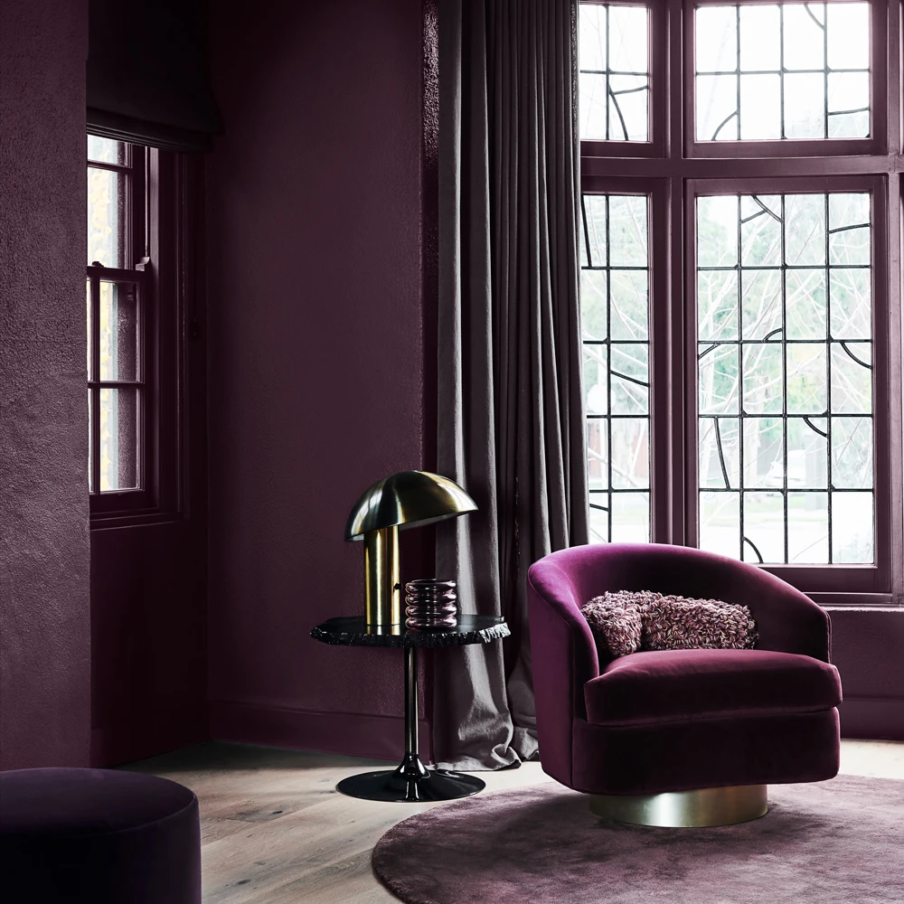 Purple reading chair in dark purple room with side table and curtains.