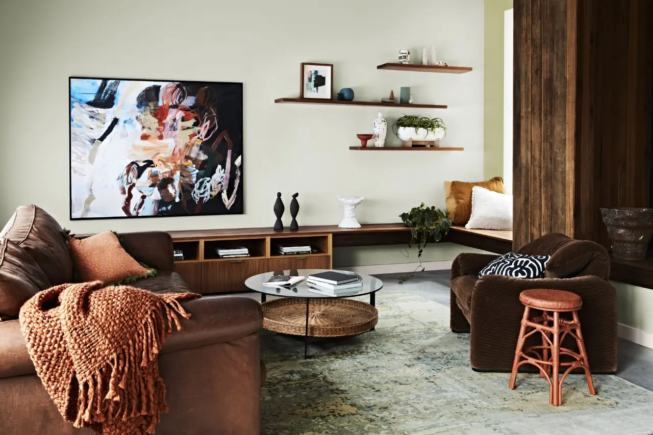 Neutral living room with brown leather couch, brown velvet armchair, knitted brown throw and timber console