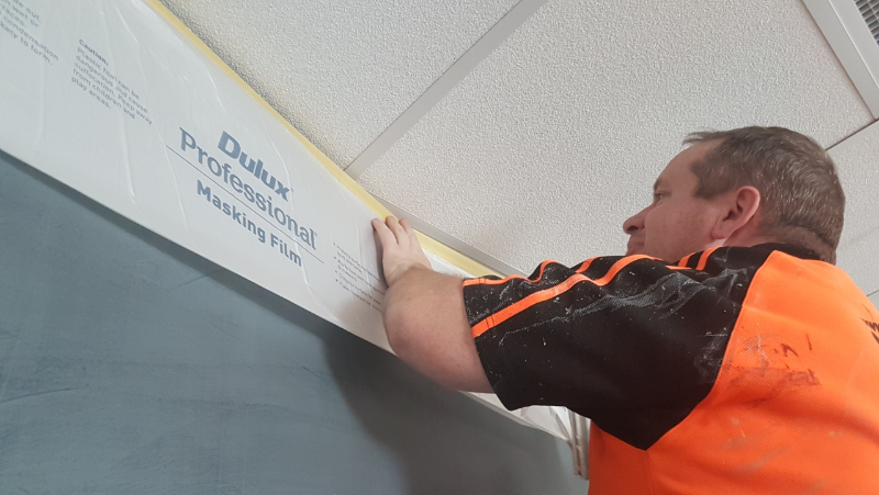 Man installing Dulux Professional Masking Film on office wall.
