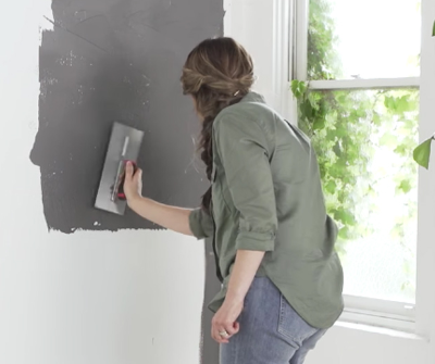 view of woman applying grey paint to white wall 
