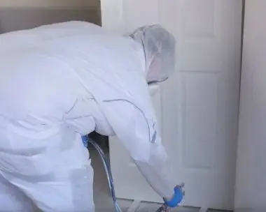 Painter in protective clothing spray painting a door