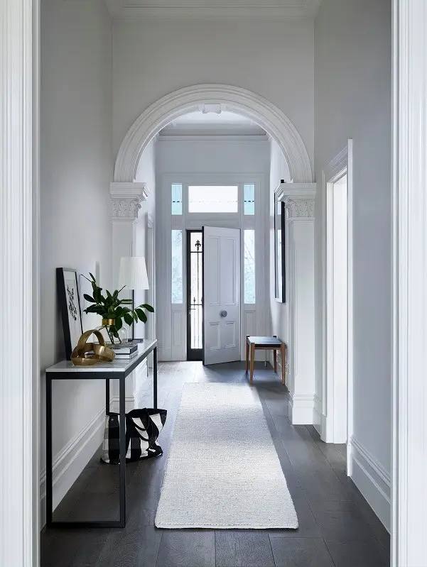 White hallway with arch feature and side table with plants on it. The white door is slightly ajar.