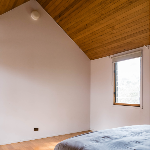 Interior bedroom featuring white wall and wooden panelling on roof before paint transformation.