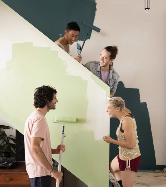 Group of young people painting a stair well two different tones of green.