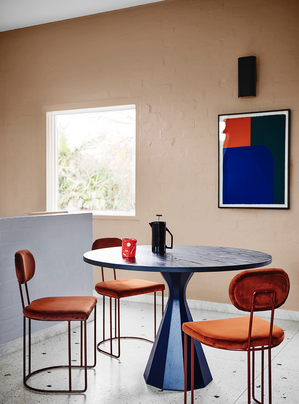 Neutral dining room with table and three chairs. There is a blue square painting on the wall with a red corner.