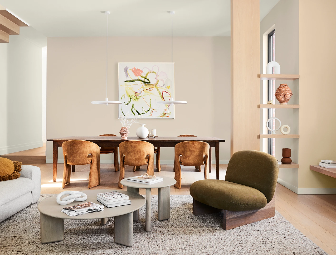 Open plan dining and living room in neutrals with large dining table and modern low armchair.