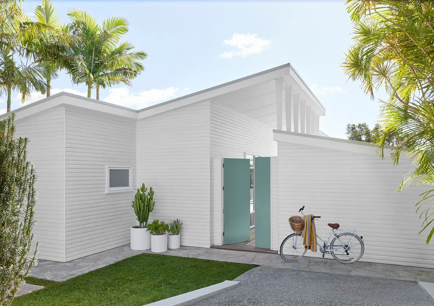 Coastal home exterior with white weatherboards turquoise front door and palm trees