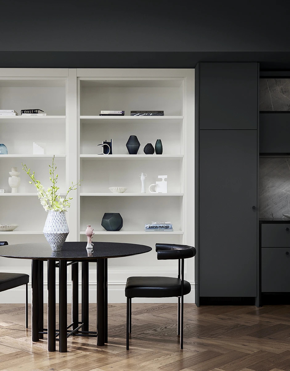 dining table on wooden floor with white built-in shelves and a dark black wall surrounding them