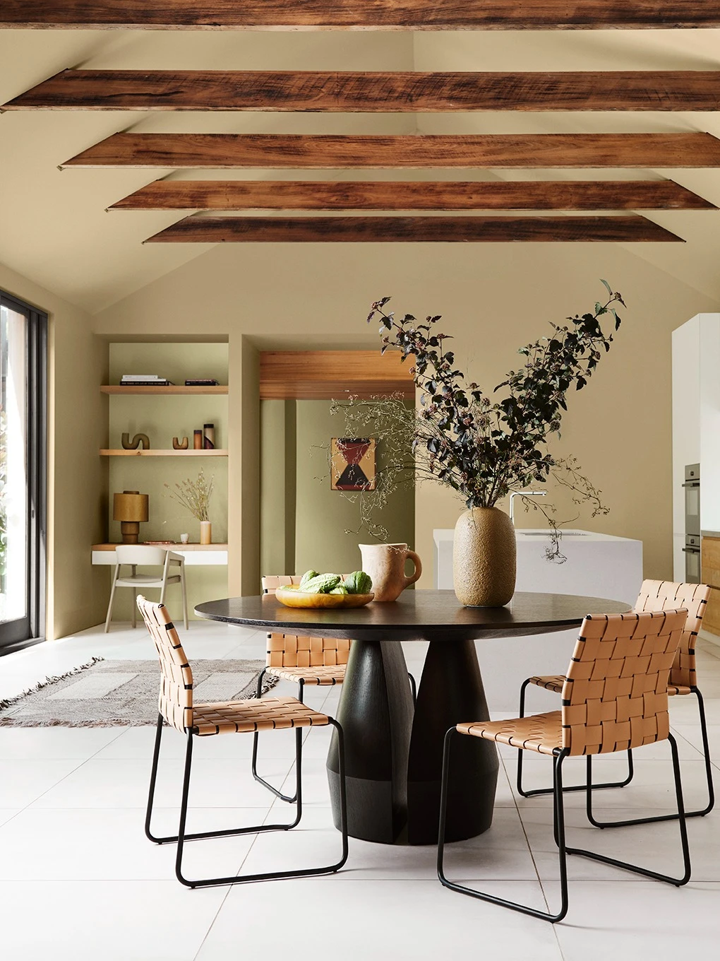 Soft green interior dining room with black round table and timber ceiling beams