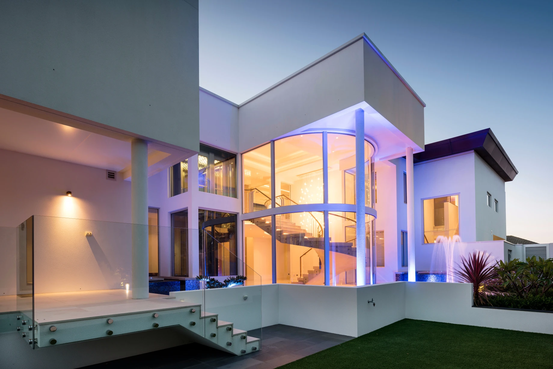 Exterior view of modern white mansion with glassed in staircase.