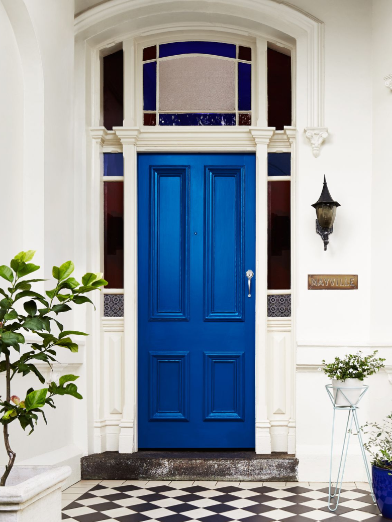 Narrow view of blue door on traditional style home with plants and checker tiles floor. 