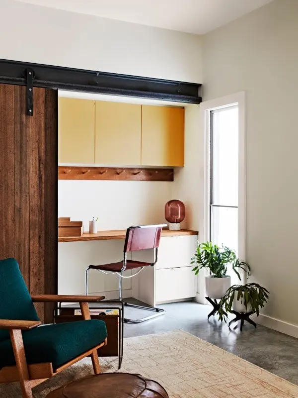 living area with a space in the corner for a desk. There are yellow cabinets above the desk and a wooden sliding door that can close the space off