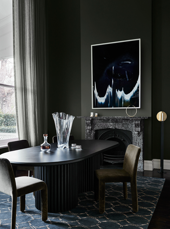 A black dining table upon a blue rug, captured in the shade of a grey wall