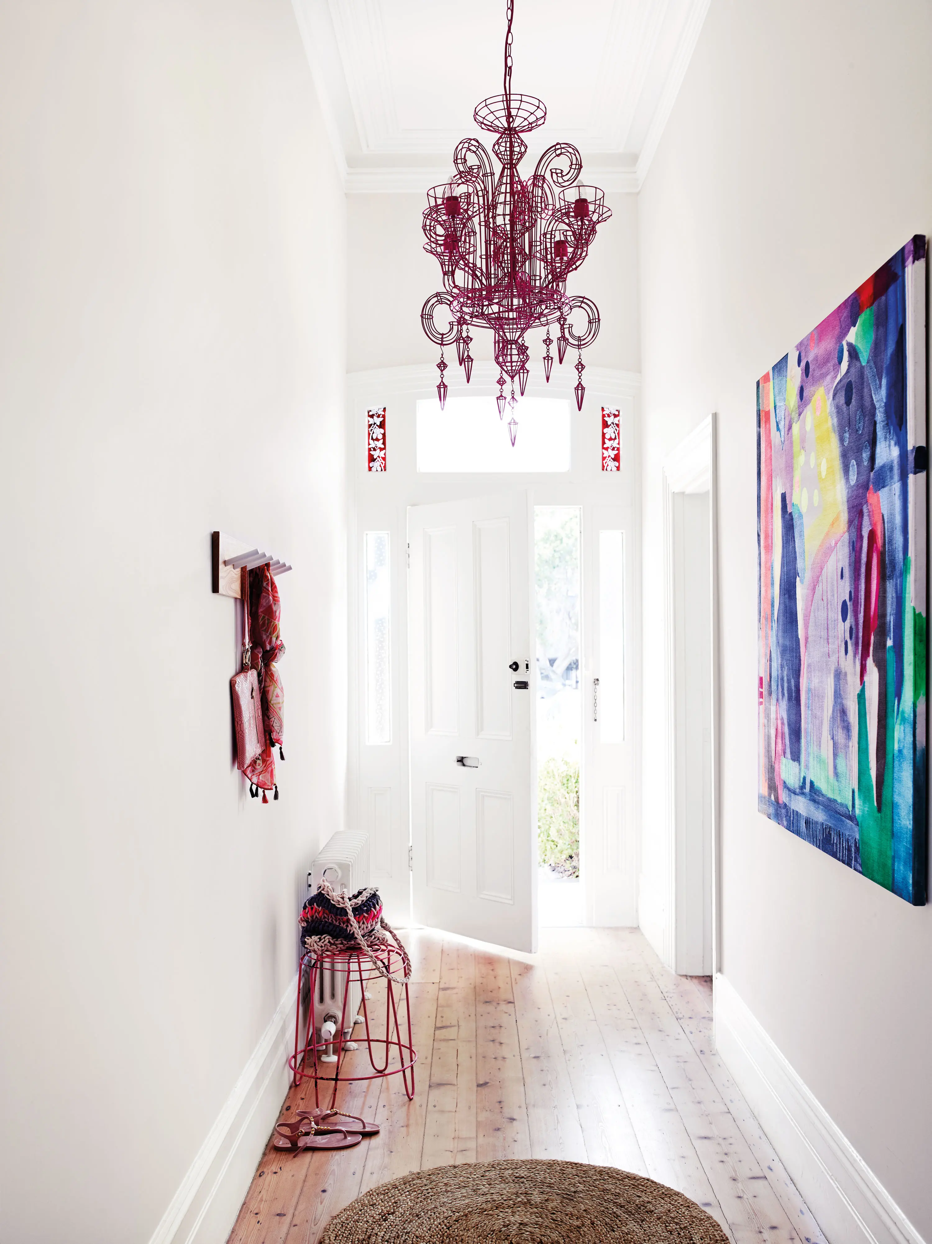 White hallway with deep red chandelier and multicoloured painting.