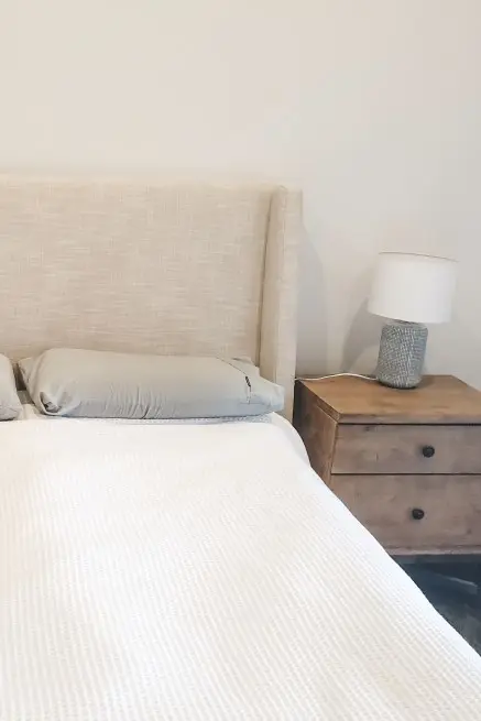 Neutral bedroom with cream suede bedhead, white doona and timber two-drawer bedside table