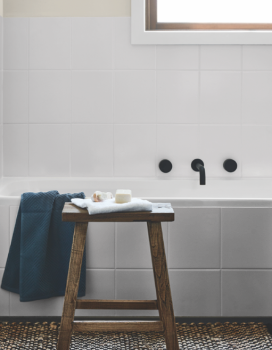 Painted white bathroom tiles with black tapware and timber stool