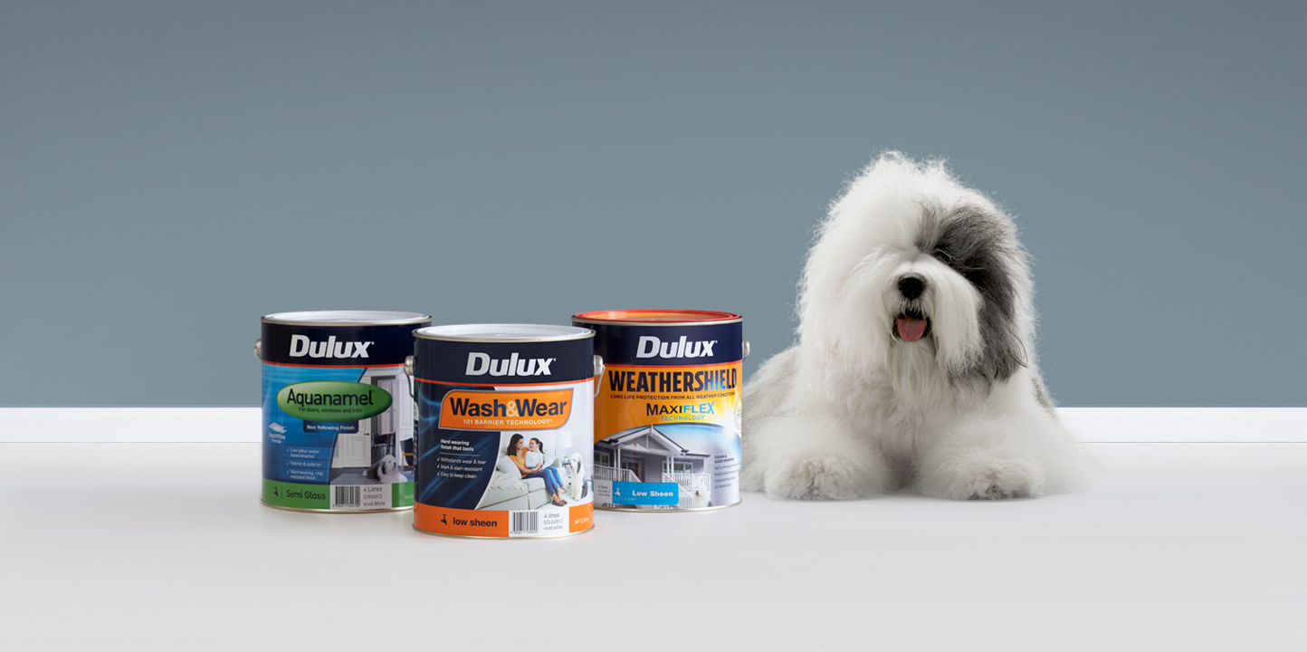 The Dulux dog lies next to Dulux products - Aquanamel, Wash&Wear, and Weathershield.