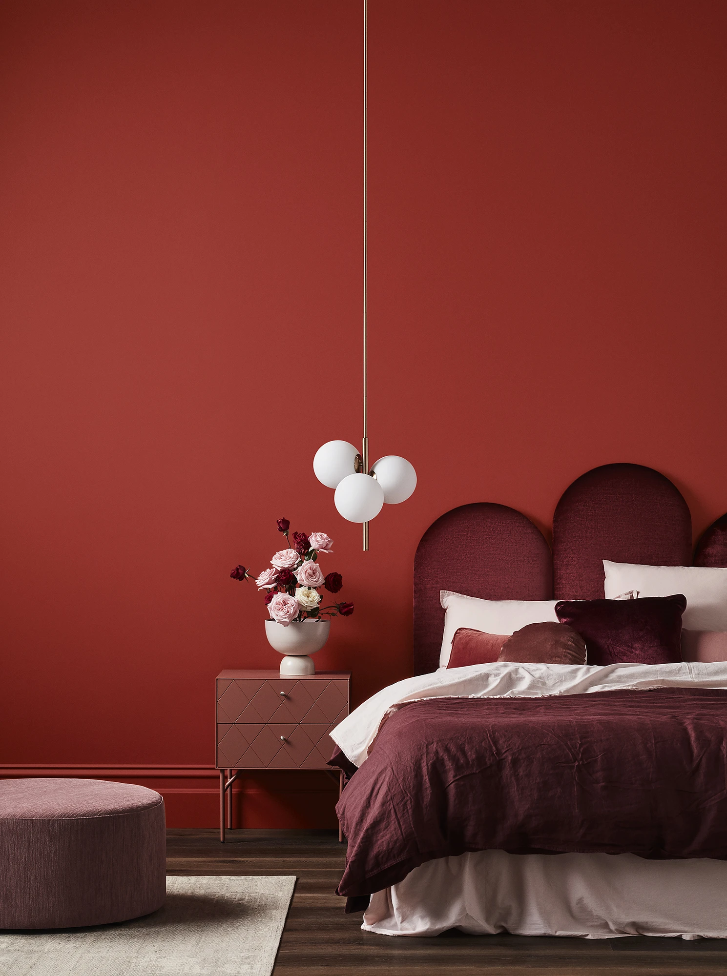 Red themed bedroom with velvet bed, bedside table and flowers in a vase.