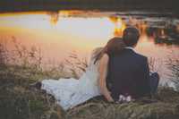 Bride and Groom sitting on the bank of a lake.