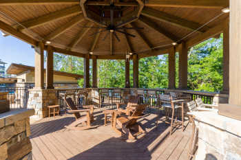 A large gazebo made of wood and stone overlooks the pool, trees, and Lake Hartwell, while Adirondack rocking chairs positioned below a large ceiling fan offer invite guests to take a load off.