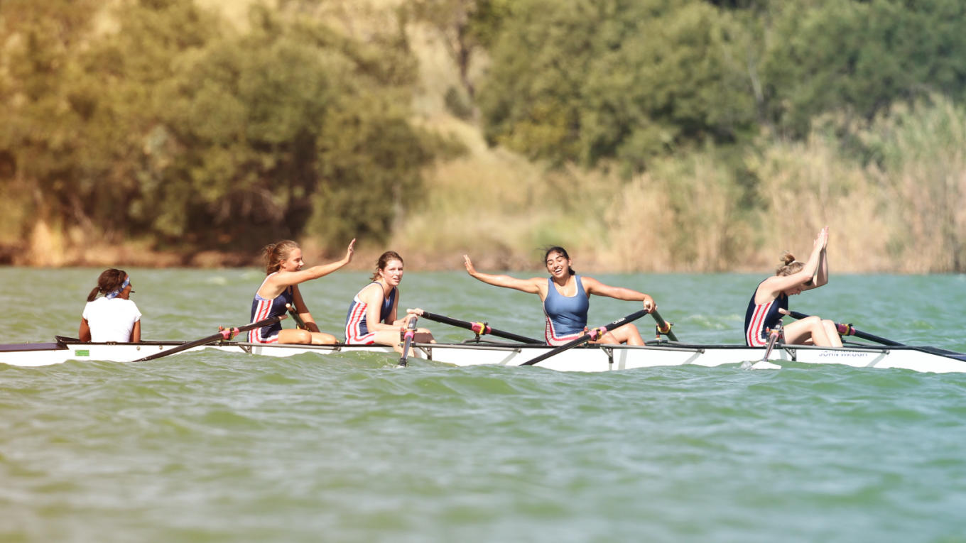 A women's crew team celebrate in their boat after a race.