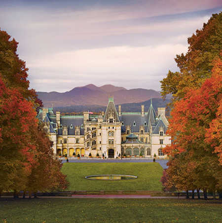 The main entrance of Biltmore is framed between autumn-colored trees, while the high peaks of the Smoky Mountains crest in the distance.