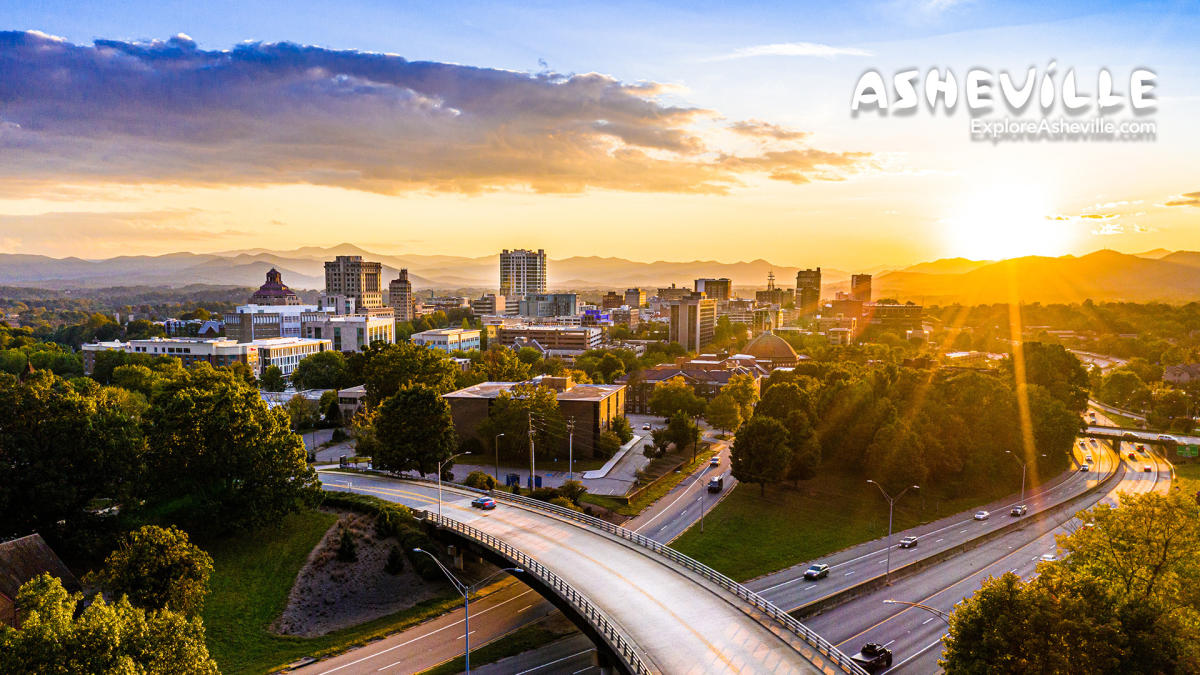 A bird's eye view of downtown Asheville as the sun sets behind the mountains.