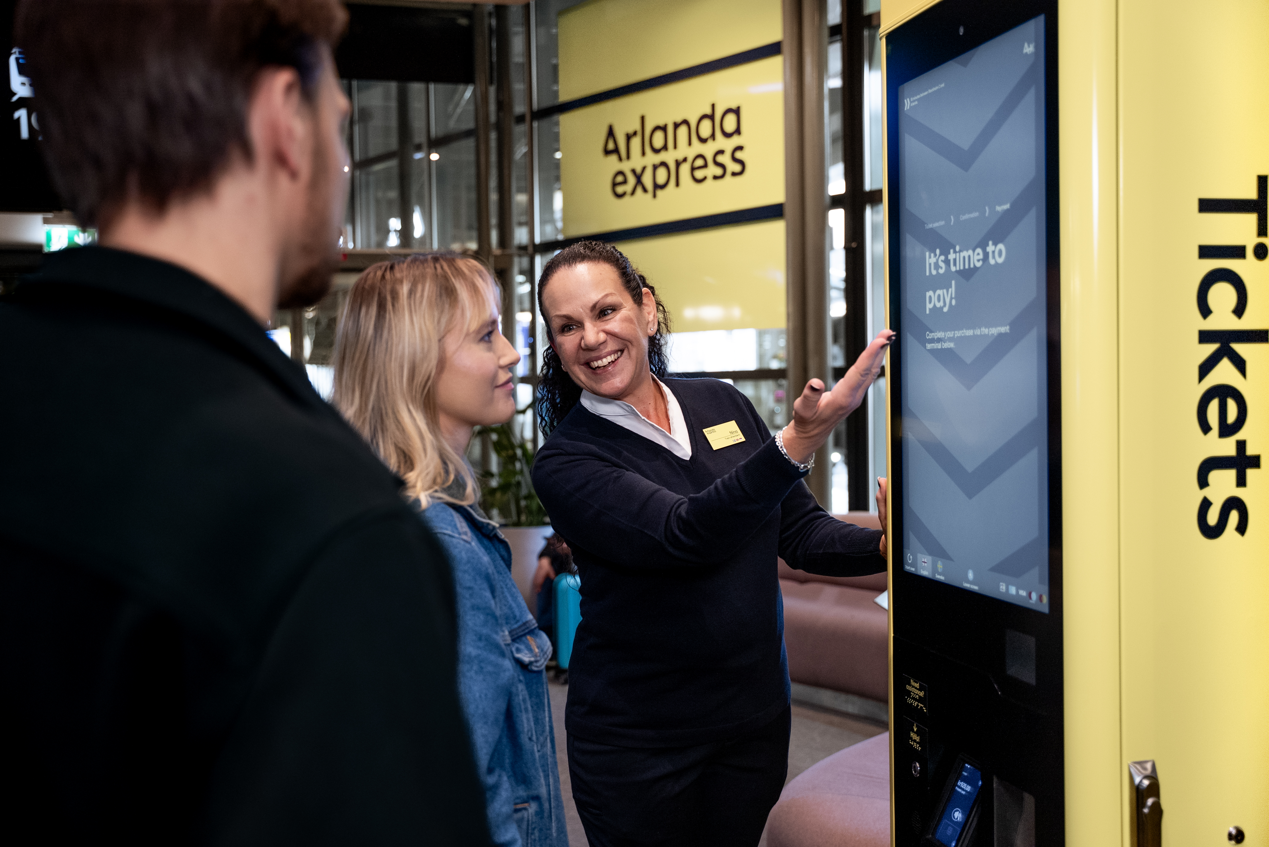 Två resenärer som får hjälp av en medarbetare vid en Arlanda Express-biljettautomat.