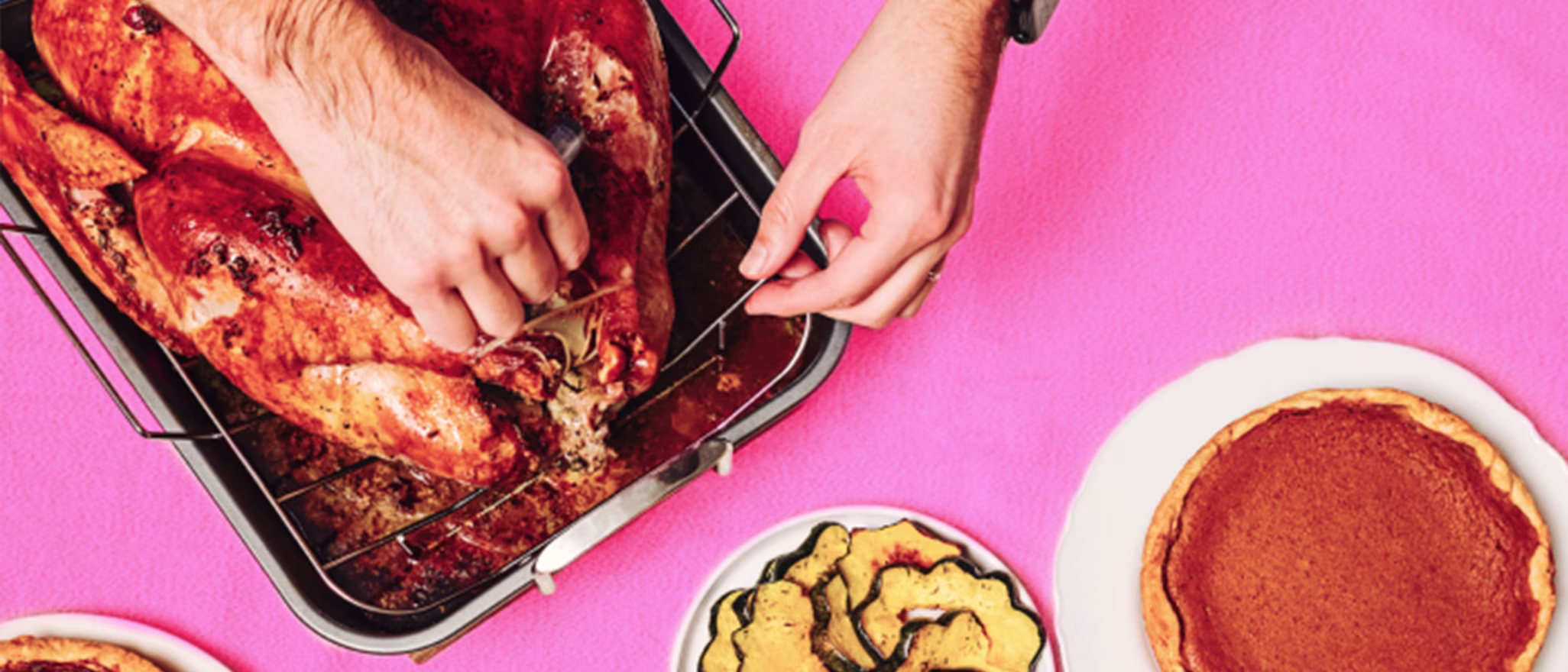 Top-down view of a person carving a roasted turkey on a table set with pies.
