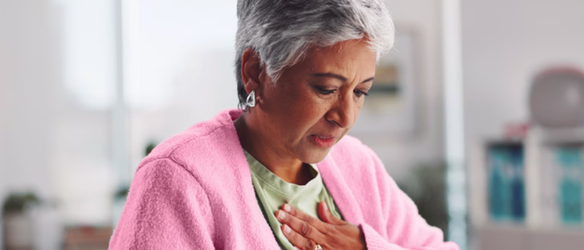An older woman looking down with a concerned expression, holding her hand to her chest to indicate heartburn.