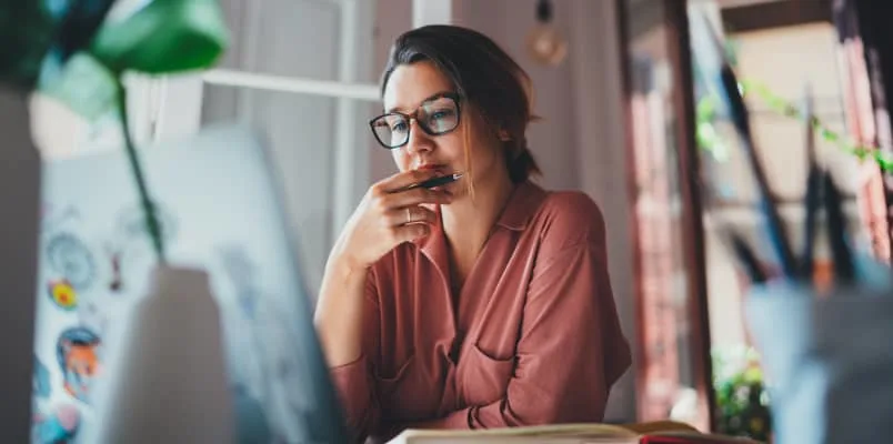 woman with glasses on computer pondering while looking at screen