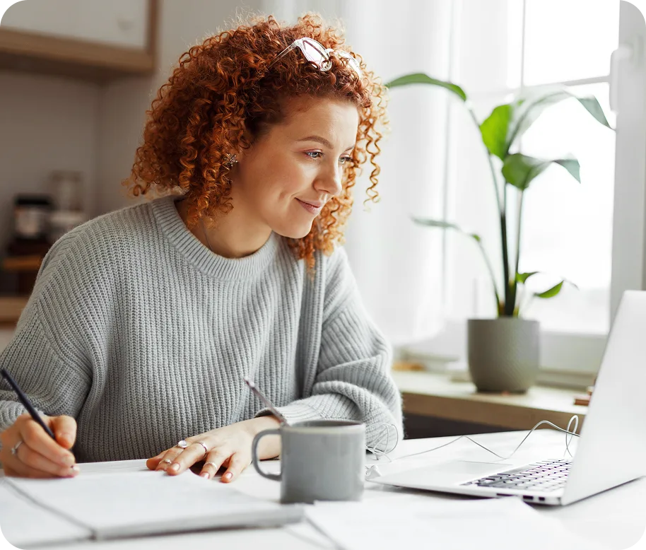 A lady smiling writing and working on laptop