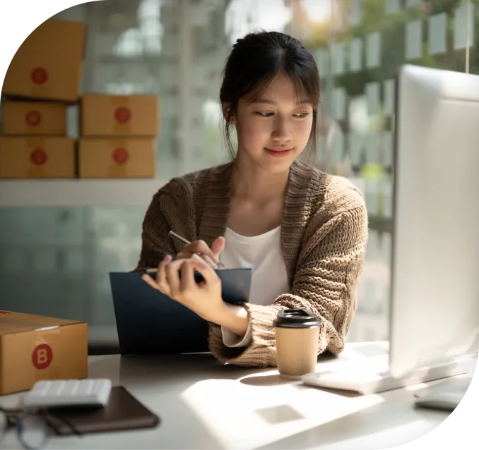 Image of a woman looking at pc while writing on a pad