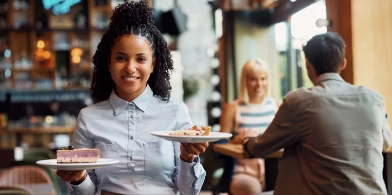 Waitress holding 2 plates of dessert in a restaurant curious how no tax on tips will affect her.