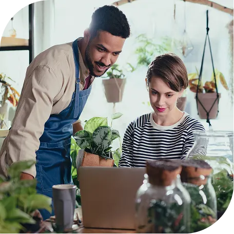 man with apron looking at a laptop of a woman in a gardening store setting