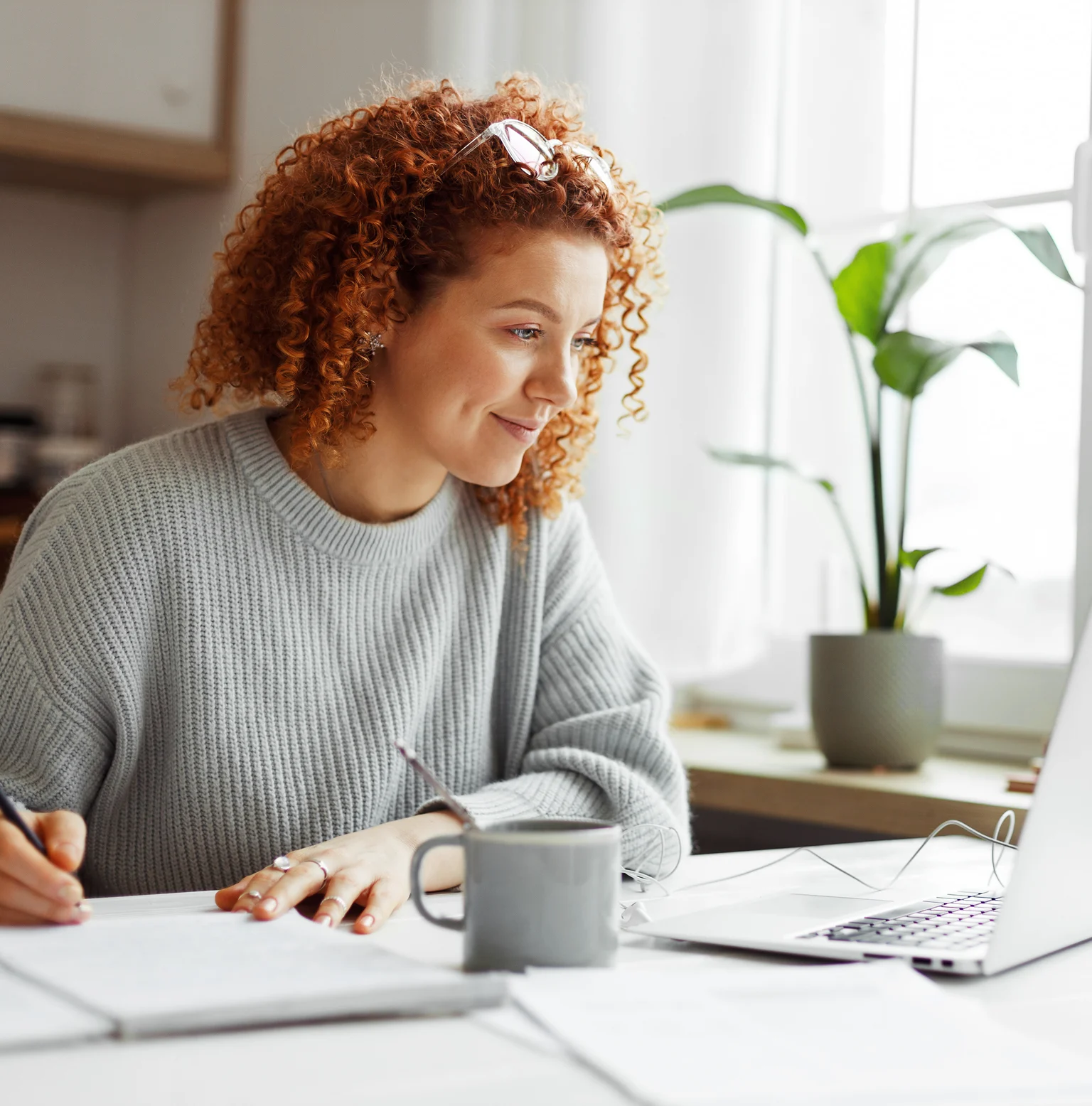 A girl smiling and looking at laptop while writing
