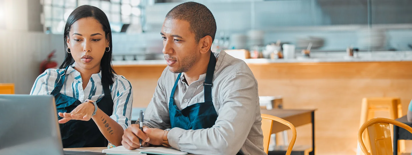 woman and man with apron discussing while looking at laptop