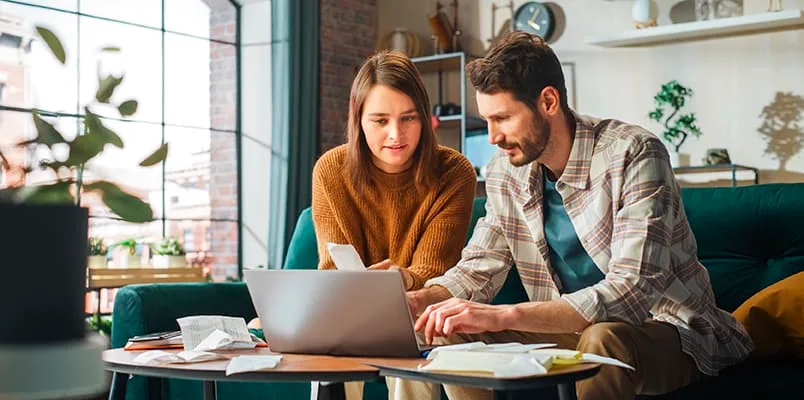 Man and woman on couch holding tax documents looking at a laptop