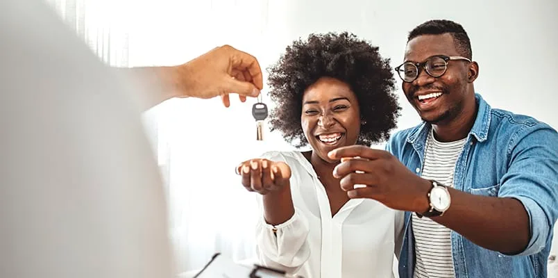 Man and woman smiling as someone hands them new keys