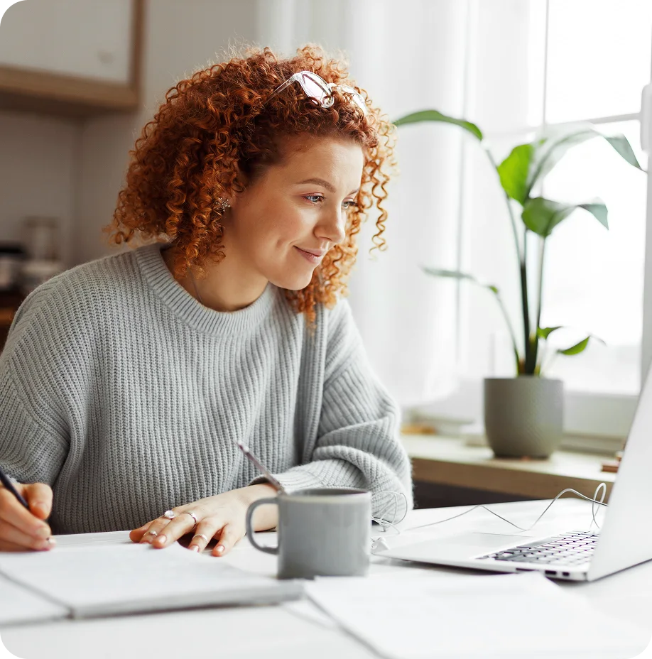 A girl smiling and looking at laptop while writing