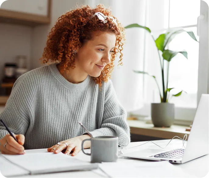 a lady writing in a note book while working on laptop
